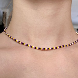 May include: A close-up of a person wearing a beaded necklace with purple, yellow, white and black beads.