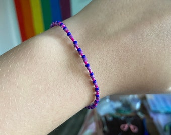 Könnte beinhalten: Ein lila und blaues Perlenarmband am Handgelenk einer Person.