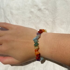 Peut inclure: Un bracelet composé de petites pierres colorées. Les pierres sont disposées en arc-en-ciel, avec des pierres rouges, orange, jaunes, vertes, bleues, indigo et violettes.