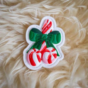 May include: White felt patch with a red and white candy cane with a green bow and the text "lick me". The candy cane is tied with a green bow. The patch is surrounded by white faux fur.