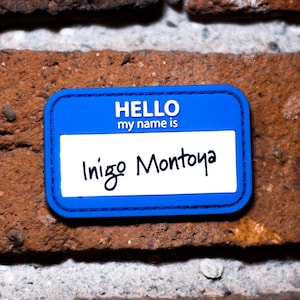 May include: Blue name tag with the text "HELLO my name is" and the handwritten name "Inigo Montoya".