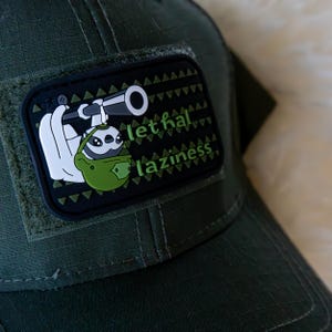 May include: A dark green baseball cap with a patch showing a cartoon sloth with a telescope, a green helmet, and the words "lethal laziness". The patch is outlined with green triangles.
