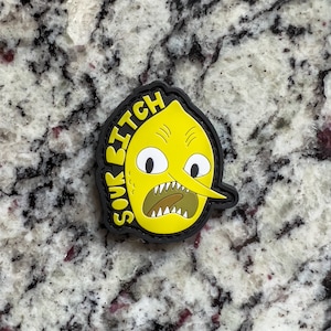 Könnte beinhalten: Ein schwarzer und gelber Patch mit einem Cartoon-Zitronengesicht und dem Text "Sour Bitch" am Rand.