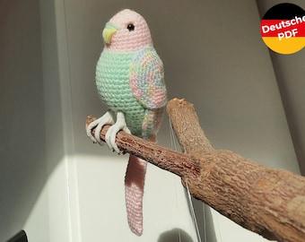 May include: A crocheted parrot with pink and green feathers perched on a branch. The parrot has a yellow beak and white feet.