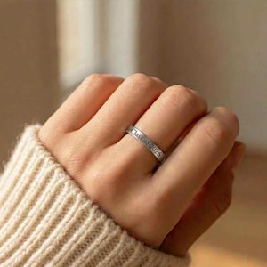 May include: A silver ring with the inscription "Class of 2026" is worn on a finger. The ring is simple and elegant, with a polished finish. The ring is a graduation or commemorative item.