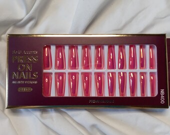 May include: A box of 24 pink press-on nails with a gold trim. The box says "Press On Nails" and "All New Designs".