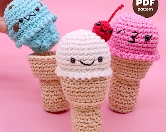 May include: Three crocheted ice cream cones with smiling faces. The ice cream cones are blue, white, and pink. The pink ice cream cone has a red cherry on top. The cones are all sitting on a pink surface. PDF pattern.