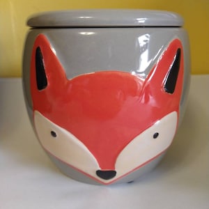 May include: A gray ceramic planter with a fox face design. The fox has orange fur, white accents around the eyes, and a black nose.