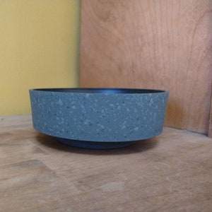 May include: A speckled gray ceramic bowl with a black rim. The bowl is sitting on a wooden surface.