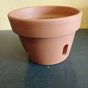 May include: A terracotta flower pot with drainage holes. The pot is a light brown color and has a smooth, slightly textured surface.