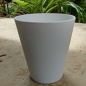 May include: A white ceramic planter with a smooth, rounded surface. The planter is empty and sitting on a light brown surface.