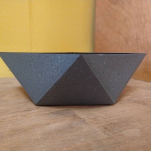 May include: A gray geometric planter with a textured surface. The planter is shaped like a star and has a wide opening.