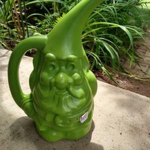 May include: Green plastic watering can shaped like a gnome with a long spout. The gnome has a white beard and a red, white, and blue sticker that says "U.S.A."