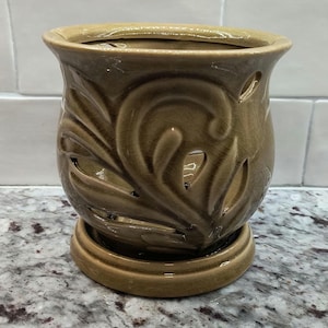May include: A ceramic candle warmer with a leafy design. The warmer is a light brown color and has a small base.