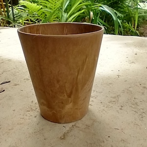 May include: A brown ceramic planter with a slightly textured surface. The planter is empty and sitting on a light brown surface.