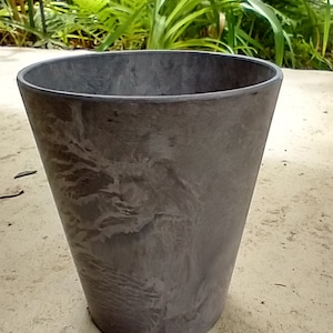 May include: A gray, textured, round planter with a wide base and a slightly tapered top. The planter is made of a durable material and has a subtle marbled effect.