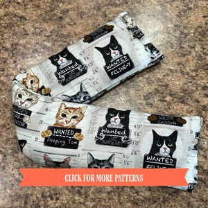 May include: Two rectangular cat-themed fabric items. The fabric features a police lineup design with various cat faces holding "Wanted" signs. The signs read "Cat Burglary", "Peeping Tom", and "Feline-Y". The text "Click for more patterns" is also visible.