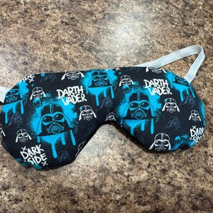 以下が含まれることがあります： 黒いスリープマスク、青と白のダース・ベイダーのデザイン。マスクには「Darth Vader」と「Dark Side」の文字が入っています。快適なフィット感のための白いゴムストラップが付いています。