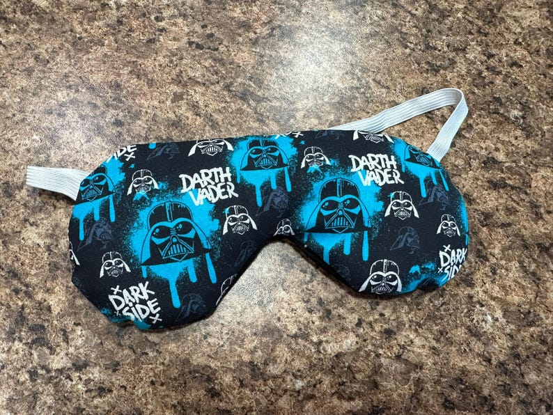 以下が含まれることがあります： 黒いスリープマスク、青と白のダース・ベイダーのデザイン。マスクには「Darth Vader」と「Dark Side」の文字が入っています。快適なフィット感のための白いゴムストラップが付いています。