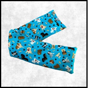 May include: A rectangular fabric pillow featuring a bright blue background with a repeating pattern of various dog breeds, small black paw prints, and light-colored bone shapes. The dogs are depicted in different colors and poses across the surface.