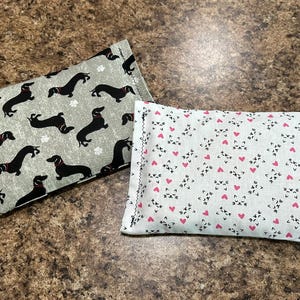 May include: Two rectangular fabric pouches. One is light gray with black dachshunds wearing red collars and white paw prints. The other is white with a pattern of pink hearts and black cat faces.
