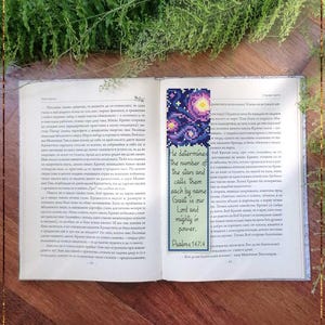 Op de afbeelding: Een geteld kruissteek-bladwijzer met een kleurrijk galaxie-ontwerp en een citaat uit Psalm 147:4: "Hij bepaalt het aantal sterren en noemt ze allemaal met hun naam. Groot is onze Heer en machtig in kracht."
