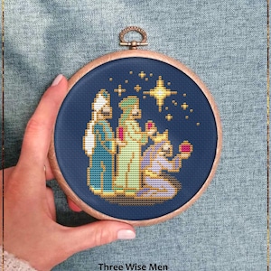 Peut inclure: Motif de point de croix des Rois Mages, présenté dans un cercle en bois. L'image montre trois personnages en robes, agenouillés sous une étoile. Le texte "Three Wise Men" et "Counted cross stitch pattern" sont en dessous.