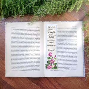 May include: Open book with a bookmark featuring a cross-stitch floral design and the text "This is love for God: to keep his commands. And his commands are not burdensome..." 1 John 5:3. The words "Bible Bookmark 1John5" are at the bottom.