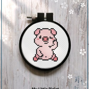 Könnte beinhalten: Ein gezähltes Kreuzstichmuster eines rosa Ferkels in einem schwarzen Stickrahmen. Das Muster trägt den Titel "My Little Piglet" und ist als PDF-Download erhältlich.