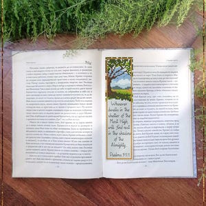 May include: Open book with a counted cross stitch bookmark. The bookmark features a tree design and the text "Whoever dwells in the shelter of the Most High will find rest in the shadow of the Almighty. Psalms 91:1."