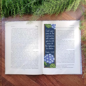 May include: A rectangular cross-stitch bookmark featuring blue hydrangea flowers at the top and bottom, with the text Cast your cares on the Lord and he will sustain you; he will never let the righteous be shaken. Psalm 55:22 in white script.