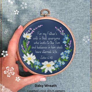 Peut inclure: Un tambour à broder circulaire en bois contenant un motif au point de croix sur tissu bleu foncé. Le motif présente une couronne florale de marguerites blanches et de fleurs bleues entourant le texte : For my Father's will is that everyone who looks to the Son and believes in him shall have eternal life. John 6:40.