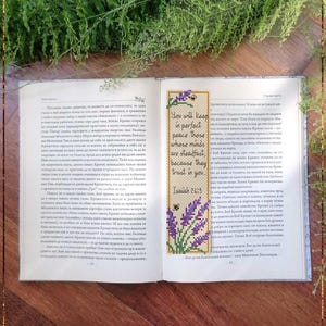 Pode incluir: Um marcador de página retangular em ponto cruz com ramos de lavanda roxos e pequenas abelhas no topo e na base. O centro contém o texto: You will keep in perfect peace those whose minds are steadfast, because they trust in you. Isaiah 26:3.