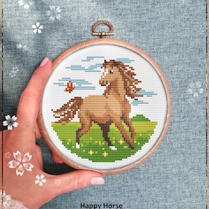 May include: A cross-stitch design of a brown horse with a flowing mane and tail, running across a green field with a butterfly. The design is set in a wooden embroidery hoop. Text reads "Happy Horse" and "Counted cross stitch pattern."