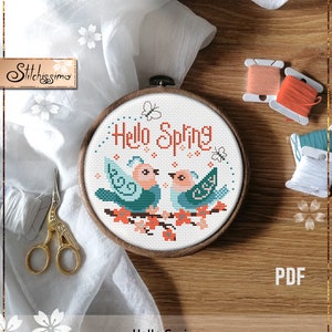 Puede incluir: Patrón de punto de cruz contado con dos pájaros azules en una rama con flores rosas. El texto "Hello Spring" está bordado en naranja sobre los pájaros.