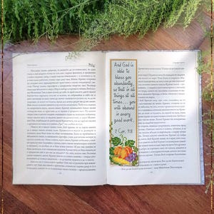 Puede incluir: Marcapáginas de la Biblia hecho a mano con un diseño de punto de cruz. El marcapáginas presenta una cita de 2 Corintios 9:8, con frutas coloridas bordadas. El texto "Bible Bookmark 2Corinthians9" está en la parte inferior.