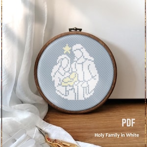 Può includere: Uno schema di punto croce contato della Sacra Famiglia in bianco, con una stella sopra, su sfondo blu. Lo schema è in un cerchio di legno e il testo "PDF Holy Family in White Counted cross stitch pattern" è sotto il cerchio.