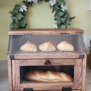 Puede incluir: Una caja de pan de madera con una puerta de vidrio y una tapa de vidrio. La caja est&aacute; llena de pan y croissants.