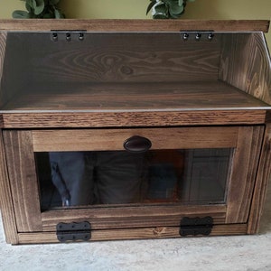 Puede incluir: Una caja de pan de madera con una puerta de vidrio y un frente de vidrio. La caja tiene un tinte marr&oacute;n oscuro y bisagras negras.