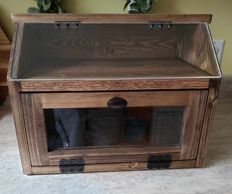 Puede incluir: Una caja de pan de madera con una puerta de vidrio y un frente de vidrio. La caja tiene un tinte marr&oacute;n oscuro y bisagras negras.