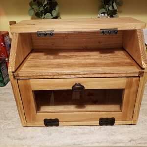 Puede incluir: Una caja de pan de madera con una puerta de vidrio y una tapa abatible. La caja tiene una perilla marr&oacute;n oscuro y bisagras negras.