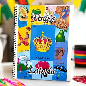 May include: Spiral-bound notebook featuring colorful illustrations from the Mexican game of Loteria. The cover displays various images, including a crown, a pear, and the text "Lotería". The notebook has a white border and a black spiral binding.