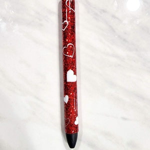 Puede incluir: Un bol&iacute;grafo rojo brillante con dise&ntilde;os de corazones blancos. El bol&iacute;grafo tiene una punta negra y detalles plateados. Es un instrumento de escritura y probablemente se utiliza para escribir diarios, tomar notas o escribir de forma creativa.