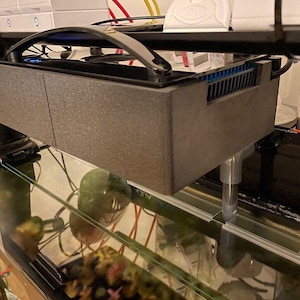 Peut inclure: Un filtre d'aquarium gris avec une poignée noire et un dessus en plastique transparent. Le filtre est monté sur le côté d'un aquarium en verre. Le filtre a une ventilation bleue.