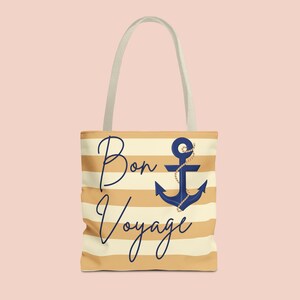 May include: A beige and white striped tote bag with a navy blue anchor design and the words "Bon Voyage" in a cursive font. The bag has a light beige handle.