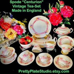 May include: A vintage Spode "Centurion" tea set. The set includes plates, cups, saucers, a sugar bowl, creamer, and a teapot. Each piece is white with a pink ribbon design and floral accents. The text "Made in England" is visible.