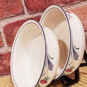 May include: Two white ceramic bowls with blue and green floral designs. The bowls are nested together and have a white background with blue and green floral designs.