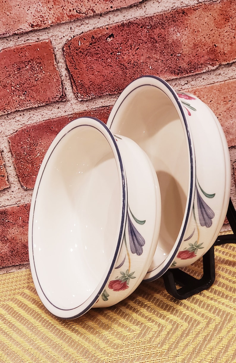 May include: Two white ceramic bowls with blue and green floral designs. The bowls are nested together and have a white background with blue and green floral designs.