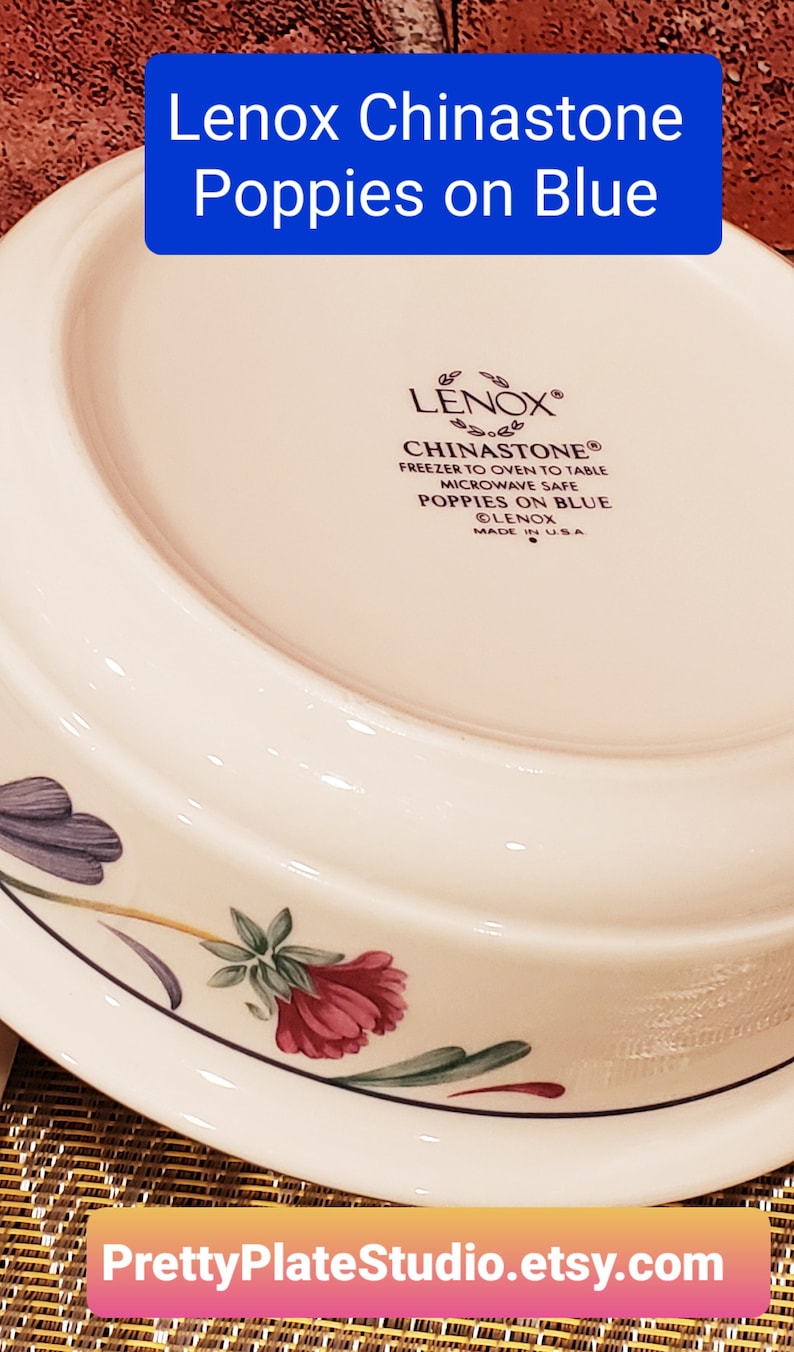 May include: A white Lenox Chinastone dinner plate with a blue and floral design. The plate features a poppy flower design with green leaves and a blue background. The plate is microwave safe and made in the USA.