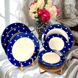 May include: A set of ceramic dinnerware featuring a deep blue rim with white polka dots and a solid cream-colored center. The collection includes several large dinner plates and smaller salad plates, all sharing the same consistent color scheme.